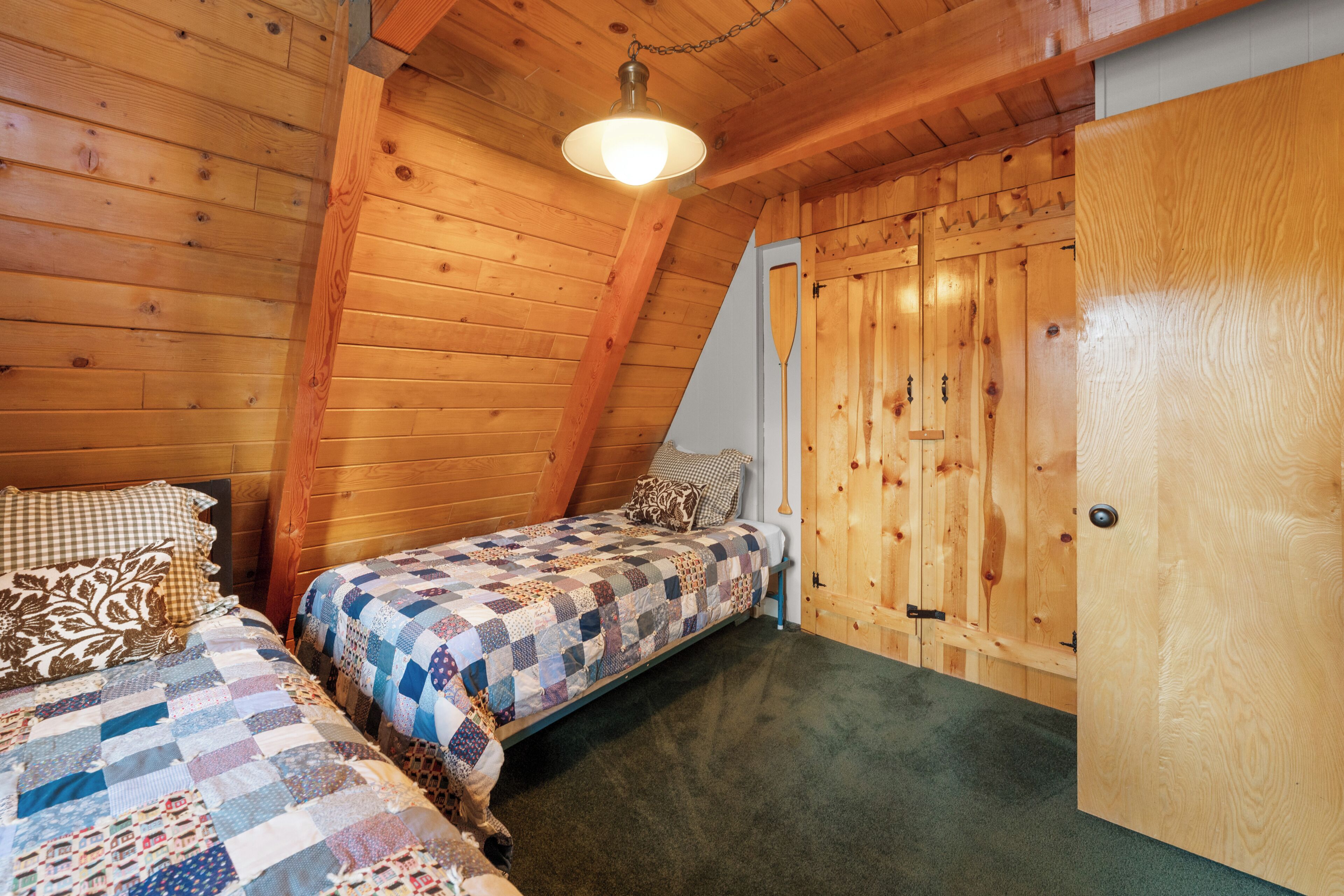 A room with two beds, wooden walls, a sloped ceiling, and a door.