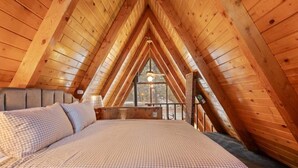 Ein Schlafzimmer mit karierter Bettdecke, Holzbalkendecke und einem Fenster mit Blick.