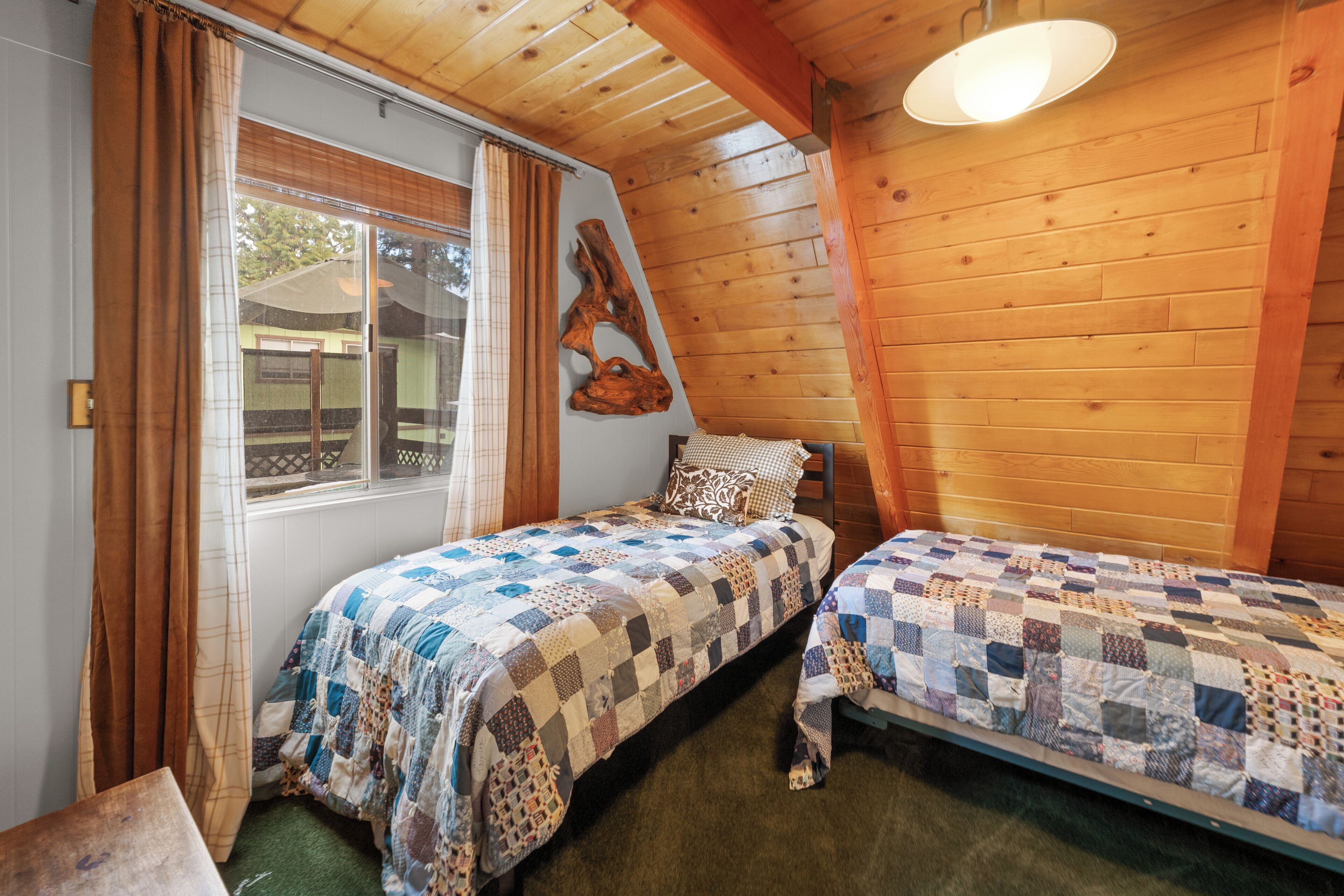 Ein Zimmer mit zwei Betten, Holzwänden, einem Fenster mit Vorhängen und einer Pendelleuchte.