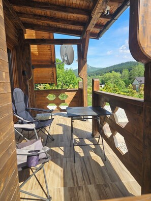 A wooden deck with a table and chairs, a satellite dish, and a view of a forested hillside.