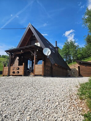 A wooden cabin with a sloped roof, a satellite dish, and a gravel driveway.