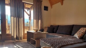 A cozy room with a sofa, a small table, a basket of folded towels, and a view through a window.