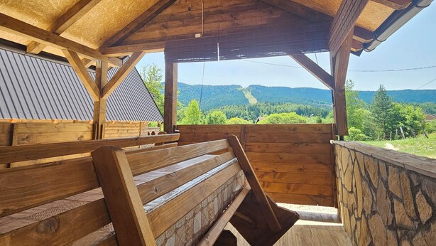 A wooden deck with benches, a stone wall, and a view of a mountainous landscape.