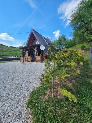 A log cabin with a gravel driveway, a satellite dish, and a view of the surrounding greenery.