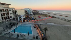 A rooftop pool with lounge chairs, a view of the beach, and a building with multiple floors. -  Atlantic's Edge @ Carolina Beach—Panoramic views of the ocean + pool /hot tub (Carolina Beach)