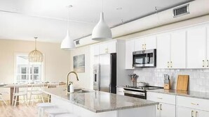 A modern kitchen with white cabinets, a marble island, stainless steel appliances, and pendant lighting. -  Atlantic's Edge @ Carolina Beach—Panoramic views of the ocean + pool /hot tub (Carolina Beach)