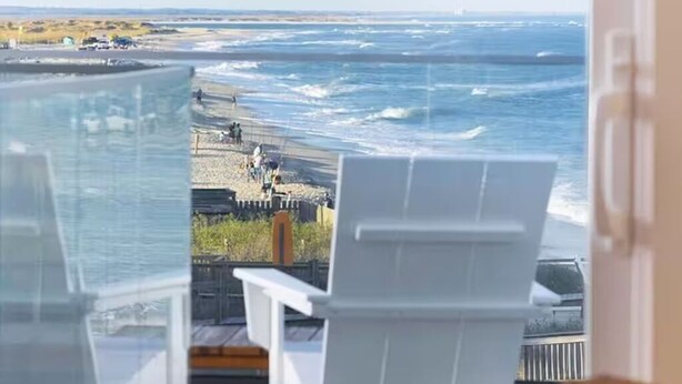 A view from a balcony overlooking the ocean with beach chairs and a railing. -  Atlantic's Edge @ Carolina Beach—Panoramic views of the ocean + pool /hot tub (Carolina Beach)