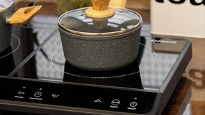 Cucina con piastre a induzione, un cucchiaio di legno, un contenitore di vetro e una pianta in vaso.