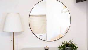 A round mirror on a wall, a lamp, a small plant, and a cabinet below. - Style and comfort studio/2 Guests/Ac/Private (Oaxaca de Juárez)