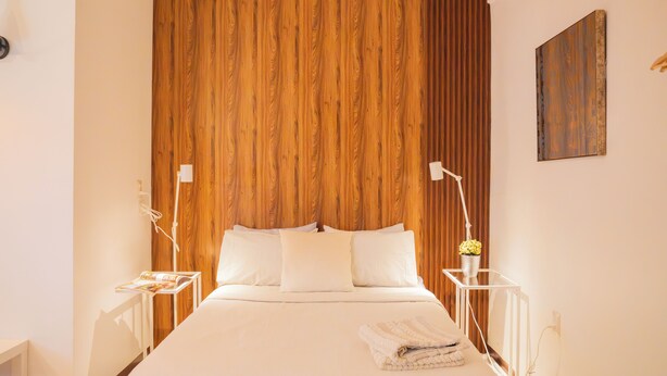 A bedroom with a wooden panel wall, a bed with white bedding, two bedside tables with lamps, and a small plant on one table. - Style and comfort studio/2 Guests/Ac/Private (Oaxaca de Juárez)
