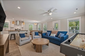 A modern living room with a blue sofa, striped chairs, a round coffee table, and a pool table.