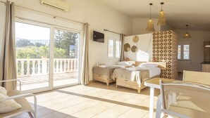 Een hotelkamer met balkon, twee bedden, een eettafel en een kitchenette.