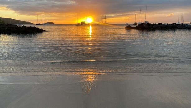 Un atardecer sobre un mar tranquilo con barcos y una costa rocosa.