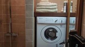 Un baño pequeño con lavadora integrada, un lavamanos y una ducha.