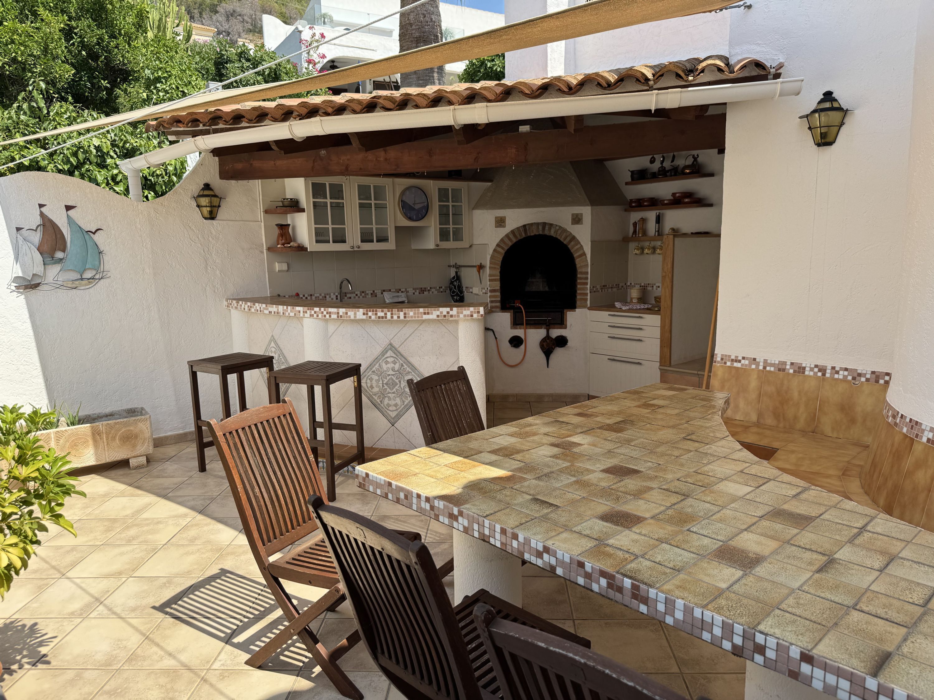 An outdoor kitchen area with a tiled countertop, wooden chairs, and a built-in oven.