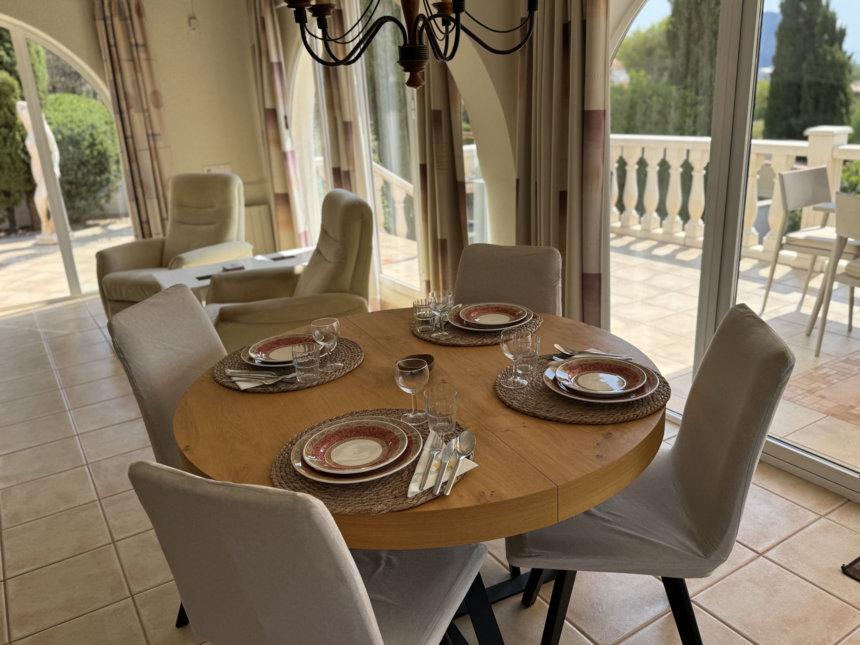 A round dining table with chairs, plates, glasses, and cutlery set for a meal.