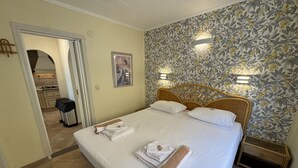 Et hotelværelse med seng, håndklæder, et træhovedgærde, blomstret tapet og et lille natbord.