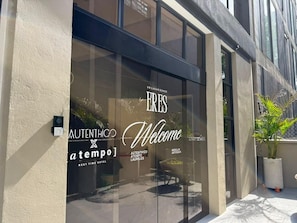 A hotel entrance with a glass facade, a welcome sign, and a security camera. - Autenthico X Atempo Local Hotel & Suites (Medellín)