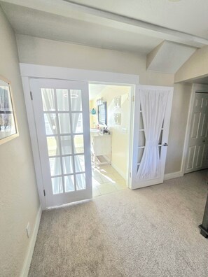 A hallway with a carpeted floor, white doors, and a bathroom visible through an open door. - The Hideaway Cottage at Second Street Cottages (Ashland)