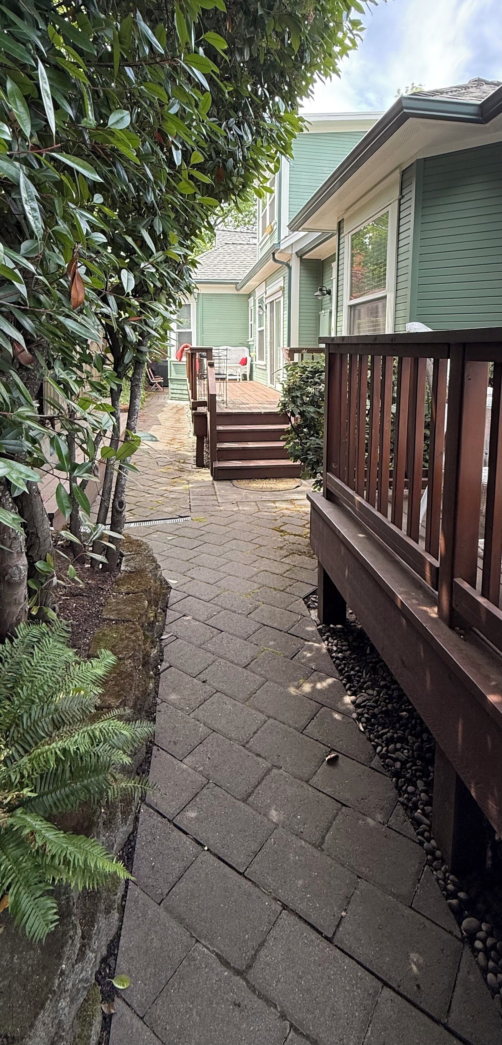 Un chemin menant à une maison dotée d’une terrasse en bois et d’une zone dallée en pierre.