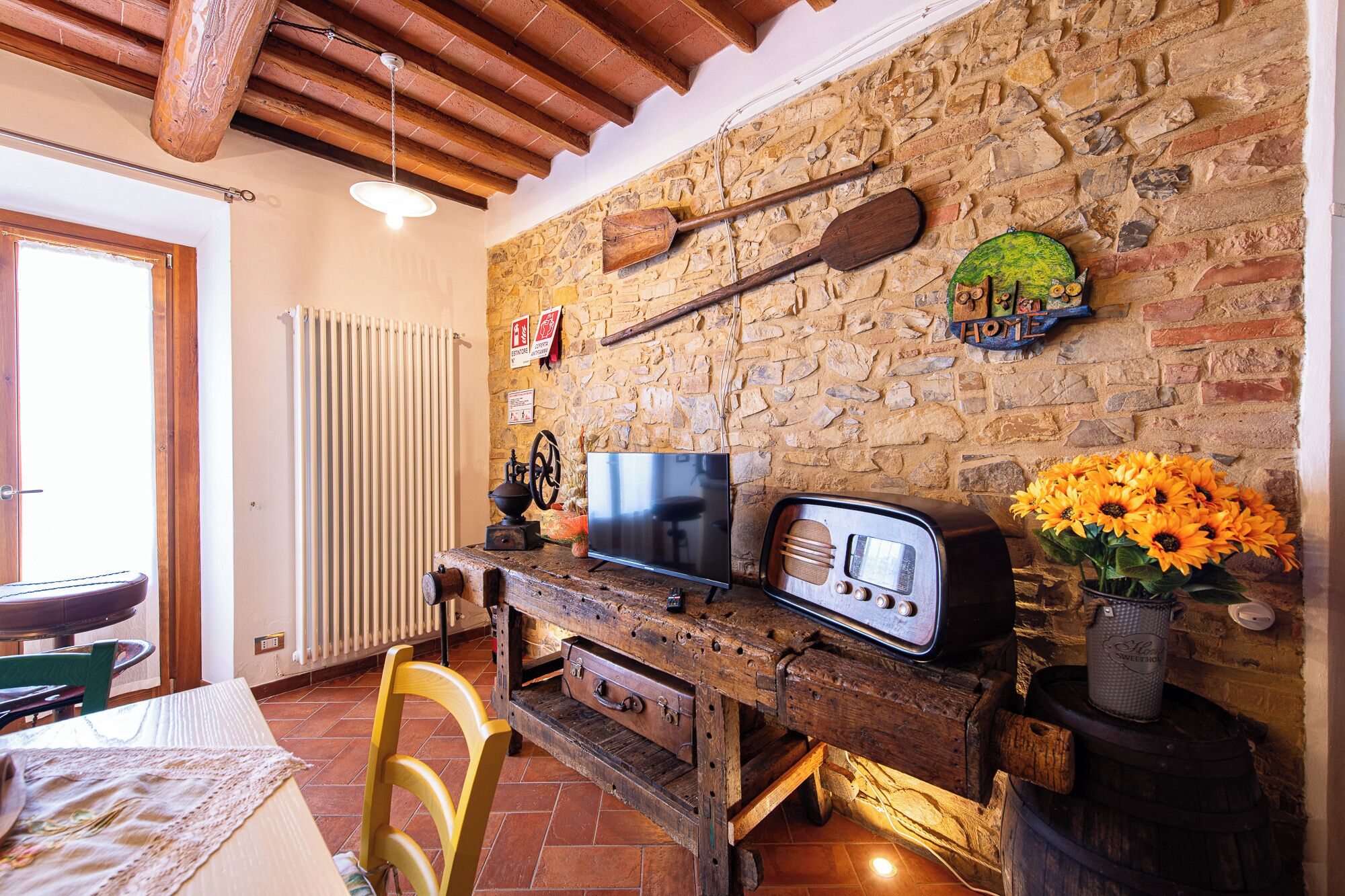 A rustic interior with a stone wall, wooden furniture, a vintage radio, and a television.