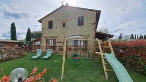 Ein Steinhaus mit einer hölzernen Spielzone inklusive Rutsche und Schaukeln.