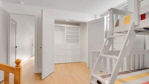 Una habitación con piso de madera, paredes blancas, una litera con escalera y un armario con varios cajones.