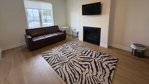 Una sala de estar con un sofá de cuero marrón, un rug con estampado de cebra, una chimenea y un televisor de pantalla plana montado en la pared.