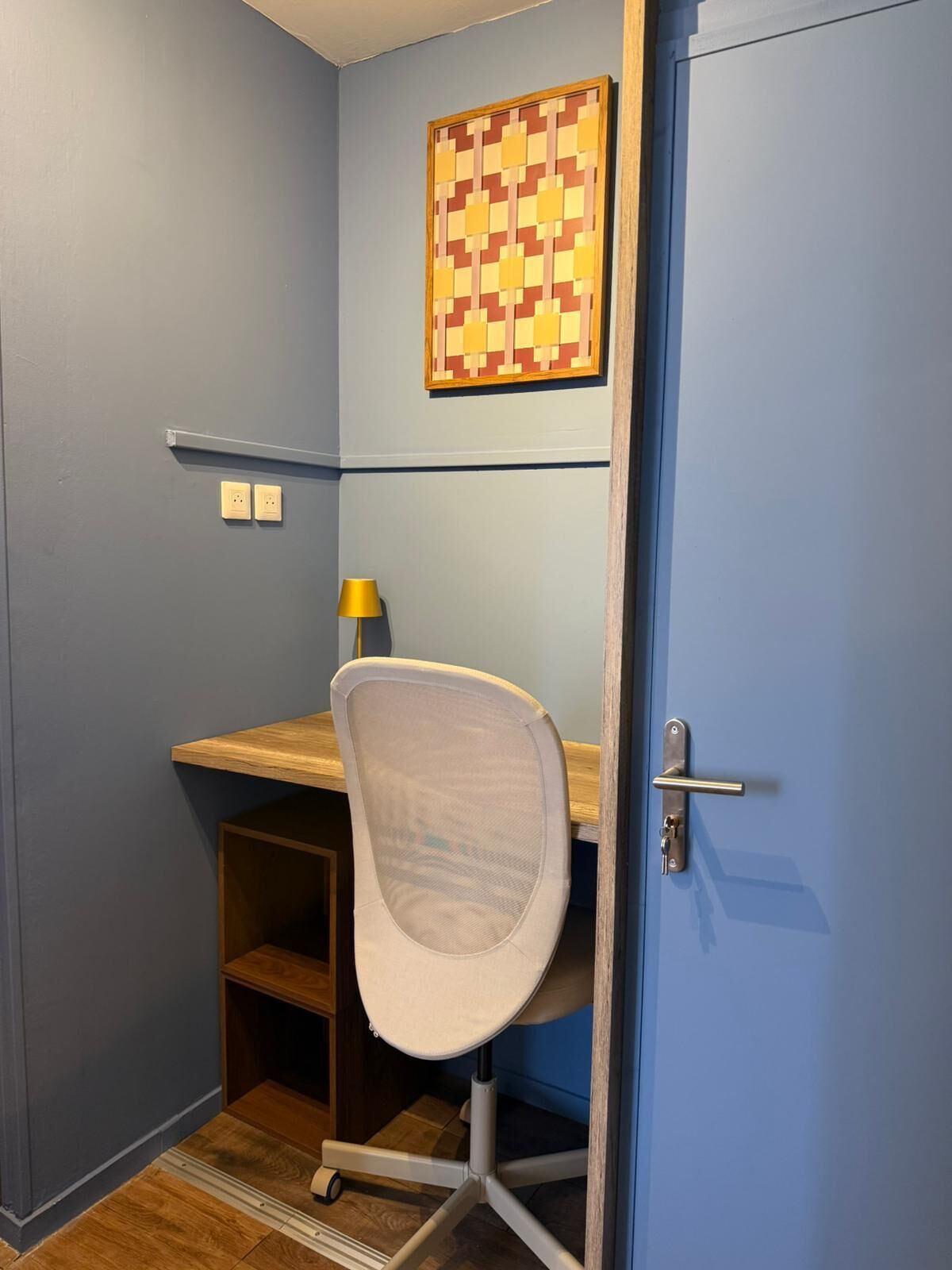 A small room with a desk, chair, lamp, and a door.
