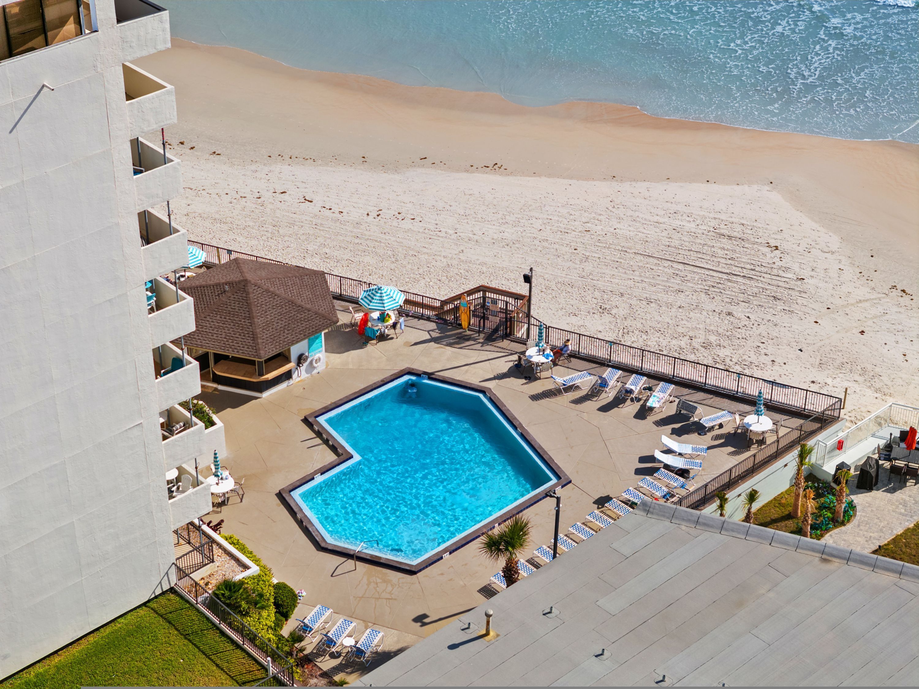 A rooftop pool with a view of the beach, lounge chairs, and a small building with a roof.