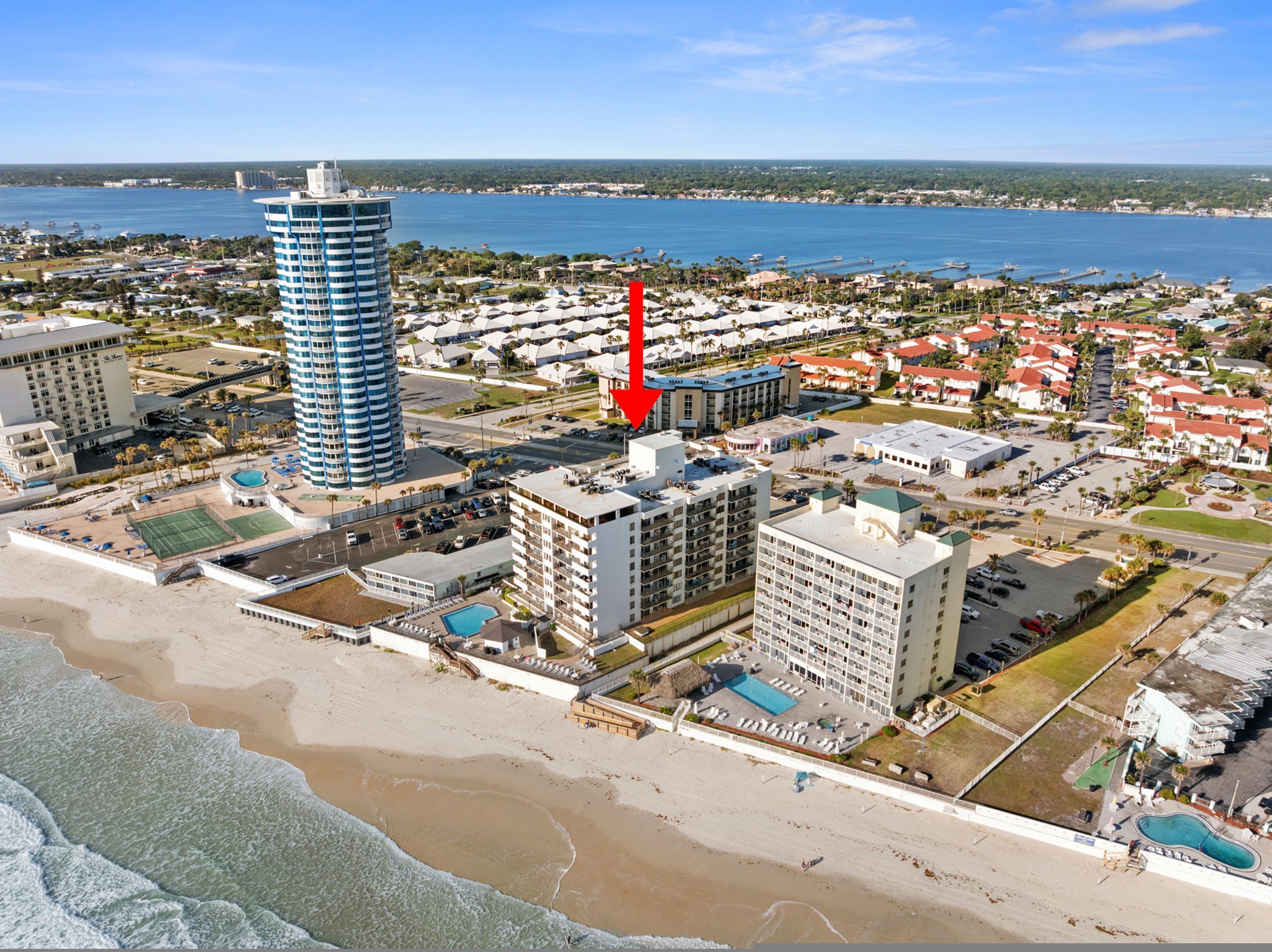 An aerial view of a coastal area with a tall hotel, a beach, and a marina.