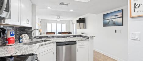 A modern kitchen with white cabinets, a stainless steel dishwasher, and a granite countertop.