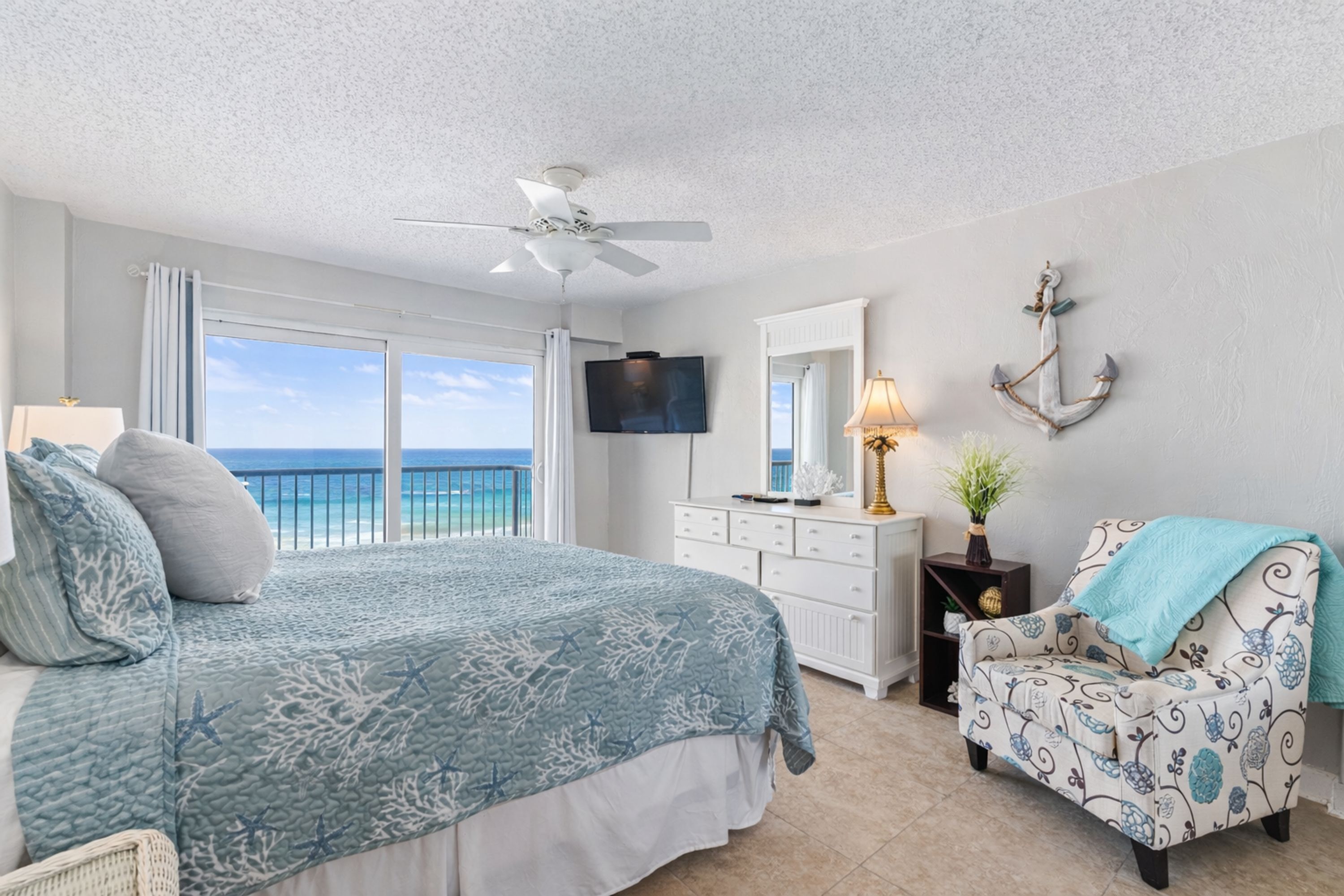 A bedroom with a bed, a chair, a TV, and a view of the ocean.