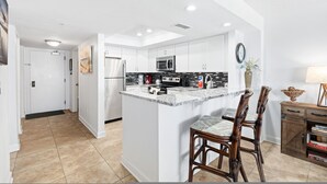 Una cocina moderna con armarios blancos, encimera de granito y un comedor con sillas de madera.