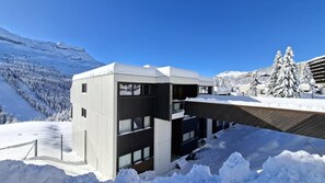 Ein modernes Gebäude mit flachem Dach, großen Fenstern und Blick auf schneebedeckte Berge.