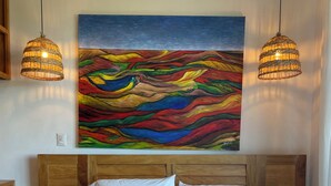 Quarto com uma cama grande, duas mesas de cabeceira, uma cabeceira de madeira e uma pintura abstrata colorida sobre a cama.
