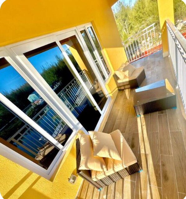 A balcony with a view of the sea, a wooden floor, and a seating area with cushions.
