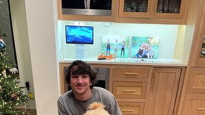 A person sitting on the floor with a dog wearing a polka dot tie, in a room with wooden cabinets, a television, and a Christmas tree. - 2-bedroom bed & breakfast in adorable Austin with AC (Austin)