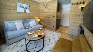 Een knus ingerichte kamer met een sofa, een bijzettafeltje met lekkernijen, een wandlamp en een houten wand.