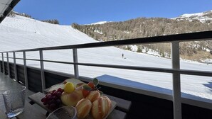 Een balkon met uitzicht op een besneeuwde berg, een tafel met fruit en een glas.