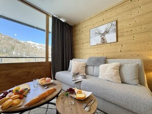 Una habitación acogedora con un sofá gris, una mesa de madera con comida y una ventana con vistas a la montaña.