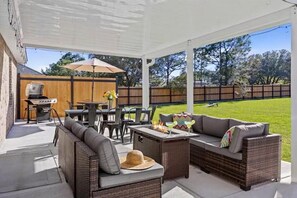 Um pátio externo com móveis de vime, churrasqueira e uma mesa com bebidas.