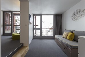 Ein modernes Zimmer mit Balkon, einer Couch mit Kissen und Holzboden.