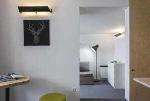 Ein modernes Zimmer mit Schreibtisch, einem grünen Hocker, einem Bett, einem Nachttisch, einer Lampe und einer Heizung.