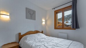 Ein Schlafzimmer mit einem hölzernen Bett, Nachttischen, Wandleuchten, einem Fenster mit Bergblick und einem Hirsch-Wandbild.