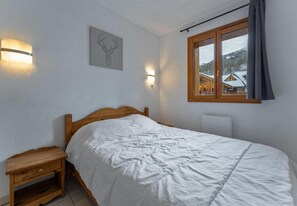 Ein Schlafzimmer mit einem hölzernen Bett, Nachttischen, Wandleuchten, einem Fenster mit Bergblick und einem Hirsch-Wandbild.