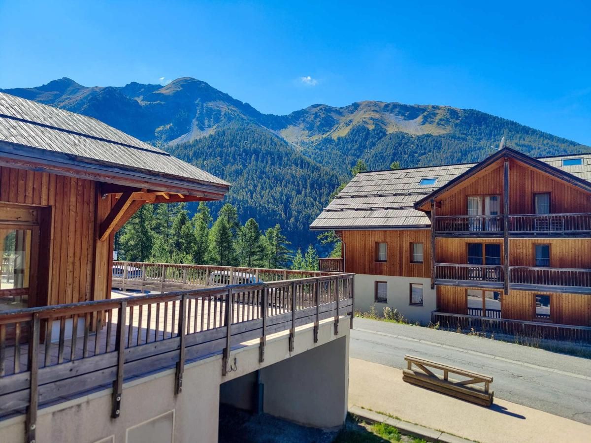 A wooden building with a balcony, a wooden bridge, and a view of mountains.