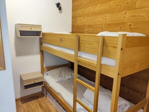 Un lit superposé avec une tête de lit en bois, une petite table de chevet et un radiateur fixé au mur.
