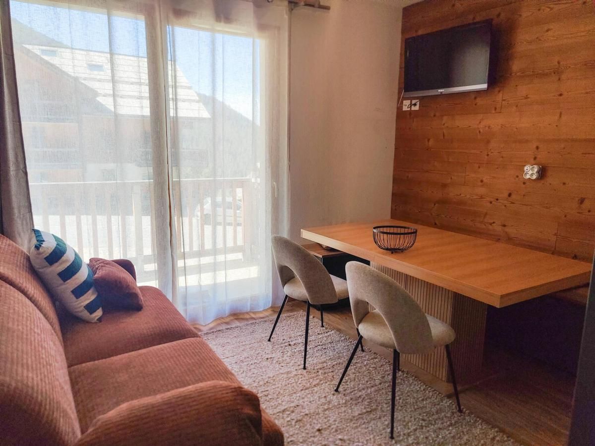 A cozy living area with a sofa, a wooden dining table with chairs, and a TV mounted on the wall.