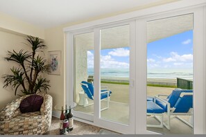 Ein Zimmer mit einer großen Schiebeglastür, die auf einen Balkon mit Liegestühlen und Meerblick führt.